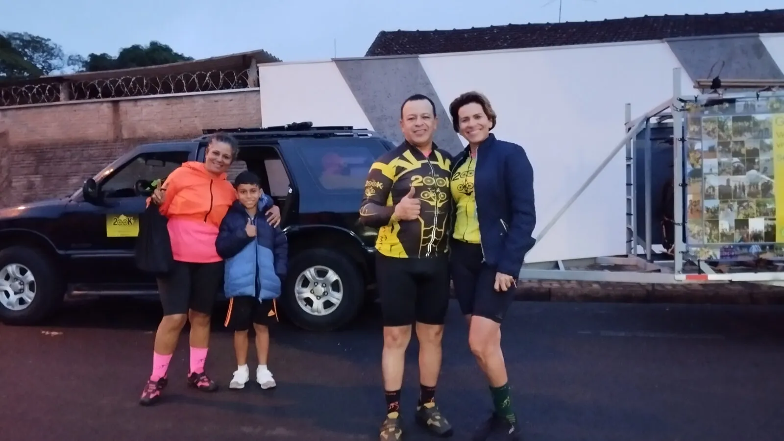 Armando e três ciclistas, entre eles uma criança, posando ao lado de uma caminhonete no começo da manhã