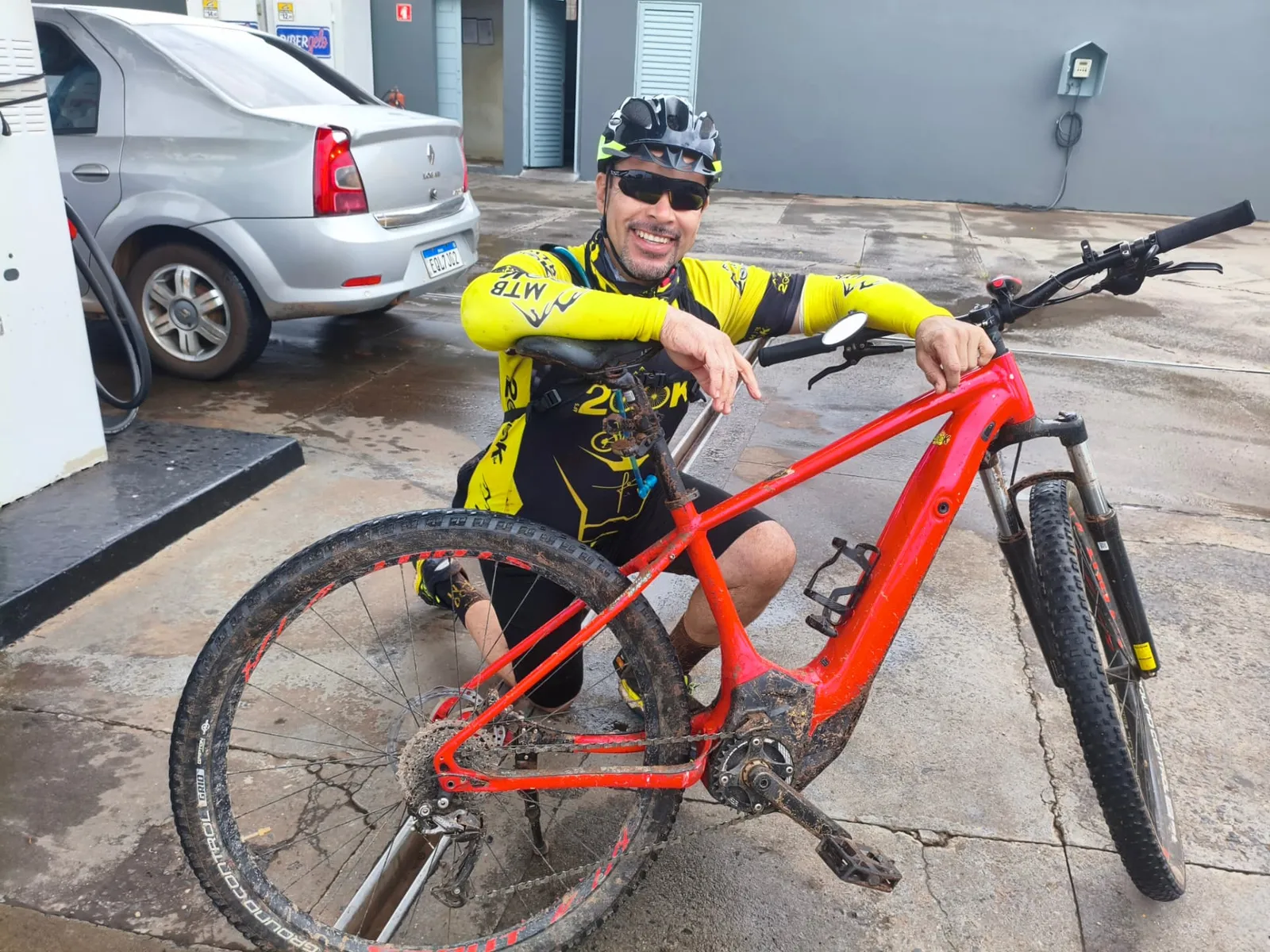 Armando de capacete e camisa do Grupo 200K, sorrindo ao lado da bike vermelha